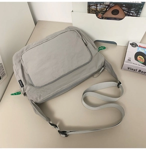 Detail of grey water-resistant nylon messenger bag with adjustable strap and side logo tag