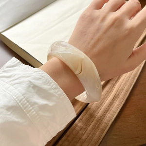Close-up of wide cream resin bangle with marble texture on female model's wrist