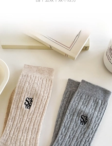 Détail de chaussettes en maille torsadée beige et grise avec écusson brodé