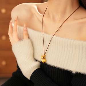 Detailed view of a brushed gold double gourd pendant necklace on a knit sweater