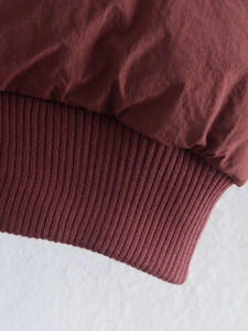Detailed macro view of dark reddish-brown stand-collar vest showing rib-knit texture and fabric