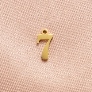 Close-up of a polished gold number 7 pendant with an integrated hanging loop for DIY jewelry