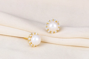 Macro shot of natural white pearl earrings with zircon halo on cream pleated fabric