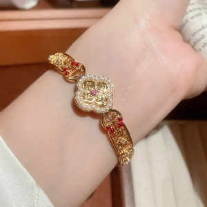 Detail of gold four-leaf clover bracelet with white pearls and red gemstones on wrist
