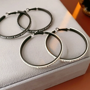 Détail de créoles rondes en cuir noir et blanc avec motifs de lettres CENIC répétés sur le bord
