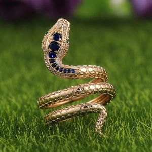 Anillo de serpiente dorado con circonitas azules y ojos verdes sobre hierba natural