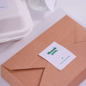 Detail of Thank You stickers applied on a brown cardboard takeaway box and white packaging