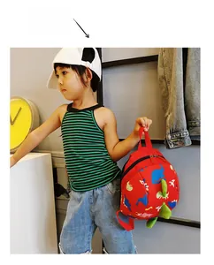 Detail of red toddler dinosaur backpack with 3D green spikes shown in a lifestyle setting