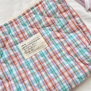 Detail of quilted plaid pouch featuring orange check pattern and attitude logo label