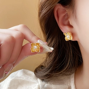 Elegant gold flower stud earrings with white pearl detail shown in hand and on model