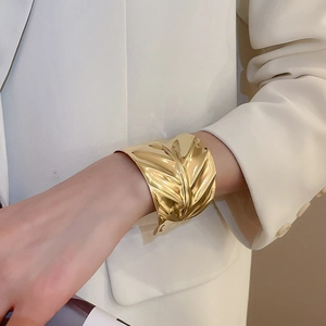 Vue détaillée du large bracelet doré à texture ondulée irrégulière sur une manche blanche