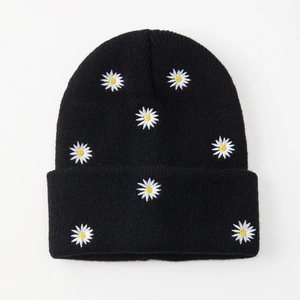 Black knit beanie with white daisy embroidery patterns on a clean white background
