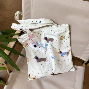Canvas tote with dachshund print, black polka dots, and a plush dog charm on a chair