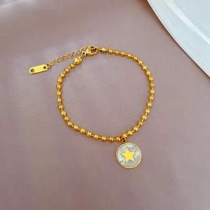 Dettaglio del bracciale in acciaio dorato con perline e ciondolo a stella in madreperla