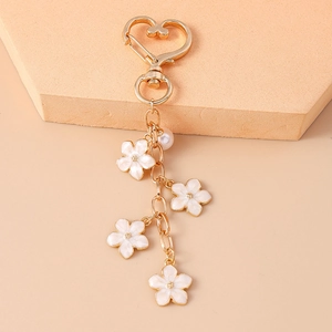 Detailed close-up of golden keychain featuring white cherry blossom charms and a pearl