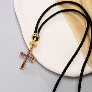 Detail of cross pendant featuring purple cubic zirconia and gold crown on black cord