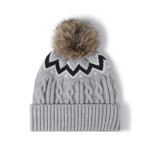 Bonnet en maille torsadée grise avec pompon en fourrure et motifs zigzag noir et blanc sur fond blanc