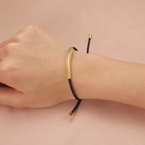 Adjustable black nylon cord bracelet with a curved matte gold stainless steel bar