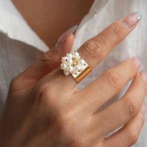 Detail of gold metal ring with white faux pearls and a central interlocking logo design