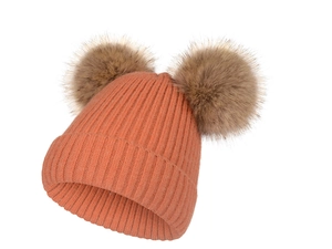 Détail du bonnet en maille orange avec deux pompons en fausse fourrure et texture douce