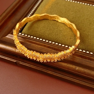 Detail of a wave-shaped gold bracelet featuring sparkling crystals on vintage velvet
