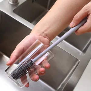 Long handle silicone bottle brush cleaning a transparent glass cup in a kitchen sink