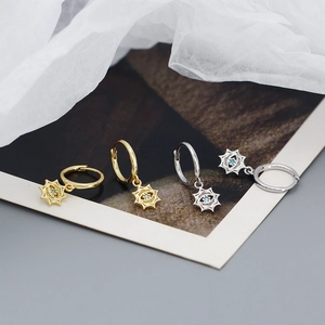 Detail of silver and gold starburst evil eye hoop earrings with green zircon accents