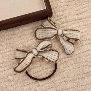 Detail of cream knitted bow hair ties and clips with dark brown stitched edges on soft fabric