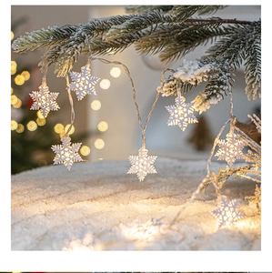 Close-up of warm white LED snowflake lights on snow-covered pine tree branches