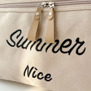 Close-up of Summer Nice black embroidery and premium leather zipper on beige canvas tote