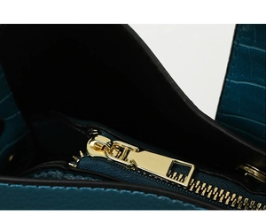 Close-up of crocodile pattern texture and gold zipper on a peacock blue handbag