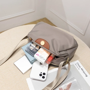 Grey nylon crossbody bag with leather trim and gold hardware in a flat lay lifestyle shot