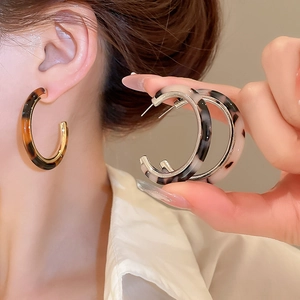 Macro detail of C-shaped resin earrings with tortoiseshell and ink patterns in a close-up view
