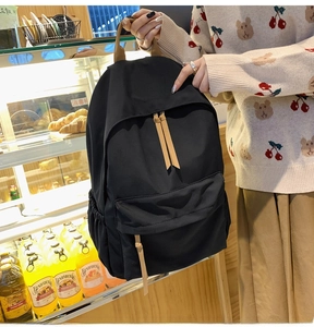 Detail of black nylon backpack featuring brown leather accents and multi-pocket design