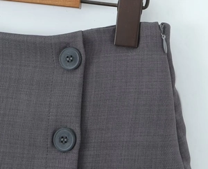 Dettaglio della gonna-pantalone a trapezio grigio scuro con bottoni a doppiopetto e zip