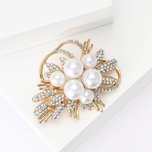 Elegant gold flower brooch with pearls and sparkling rhinestones on a white pedestal