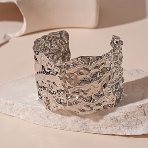 Macro shot of silver wide open cuff bracelet with lava texture on white stone base