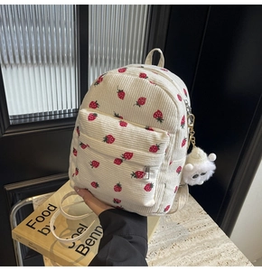 Detail view of corduroy backpack featuring red strawberry patterns and plush charm