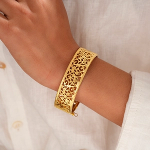 Detail of vintage gold hollowed-out pattern bracelet worn on wrist over white linen