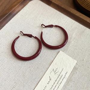 Detail view of geometric wine red round hoop earrings on a textured fabric and wooden tray