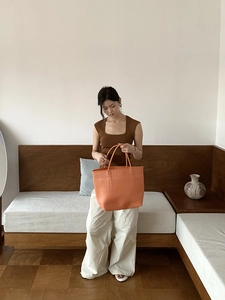 Detailed view of an orange woven straw tote bag held by a model in a minimalist setting