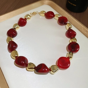 Detail of acrylic dyed irregular red and gold beads necklace on a luxury white tray