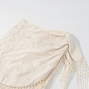 Détail de jupe en dentelle beige avec broderie florale délicate et glands tressés