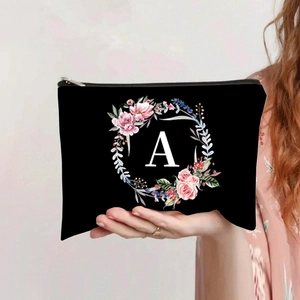 Handheld view of black canvas pouch with floral wreath design and white letter A detail