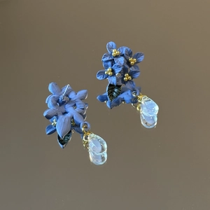 Close-up of blue flower earrings with gold stamens and a transparent water drop pendant