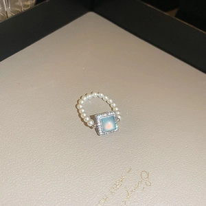 Close-up of pearl ring with light blue square stone and diamond halo on beige tray