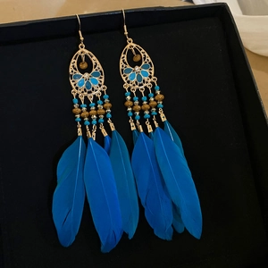 Détail de boucles d'oreilles bohèmes en plumes bleues avec filigrane doré et perles
