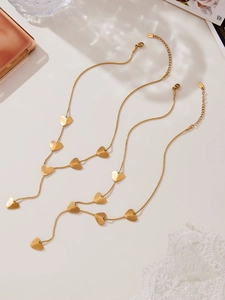 Detail of two gold plated stainless steel heart necklaces on a warm minimalist background