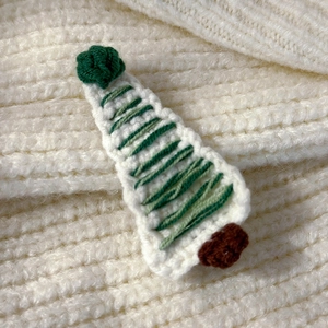 Detailed close-up of handmade crochet Christmas tree hair clip on knit fabric texture