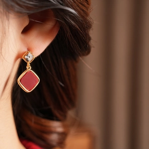 Close-up of 18k gold plated diamond-shaped earrings with red cubic zirconia on ear